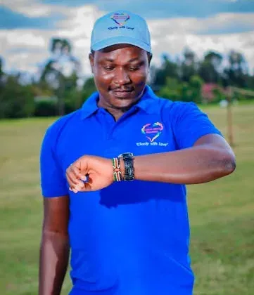Bernard Karanja in a blue polo shirt on a playing field, checking his watch