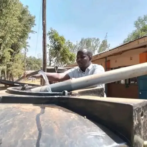 Bernard Karanja filling a large water tank at a Foundation water project